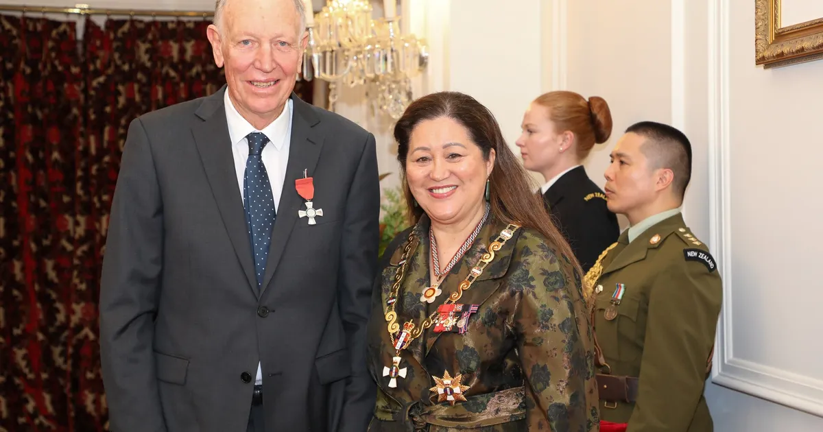 Äldre man i mörkblå kostym med medalj bredvid kvinnan i militär ceremonidräkt med guldkedjor och medaljer, i elegant salong med kristallkrona.